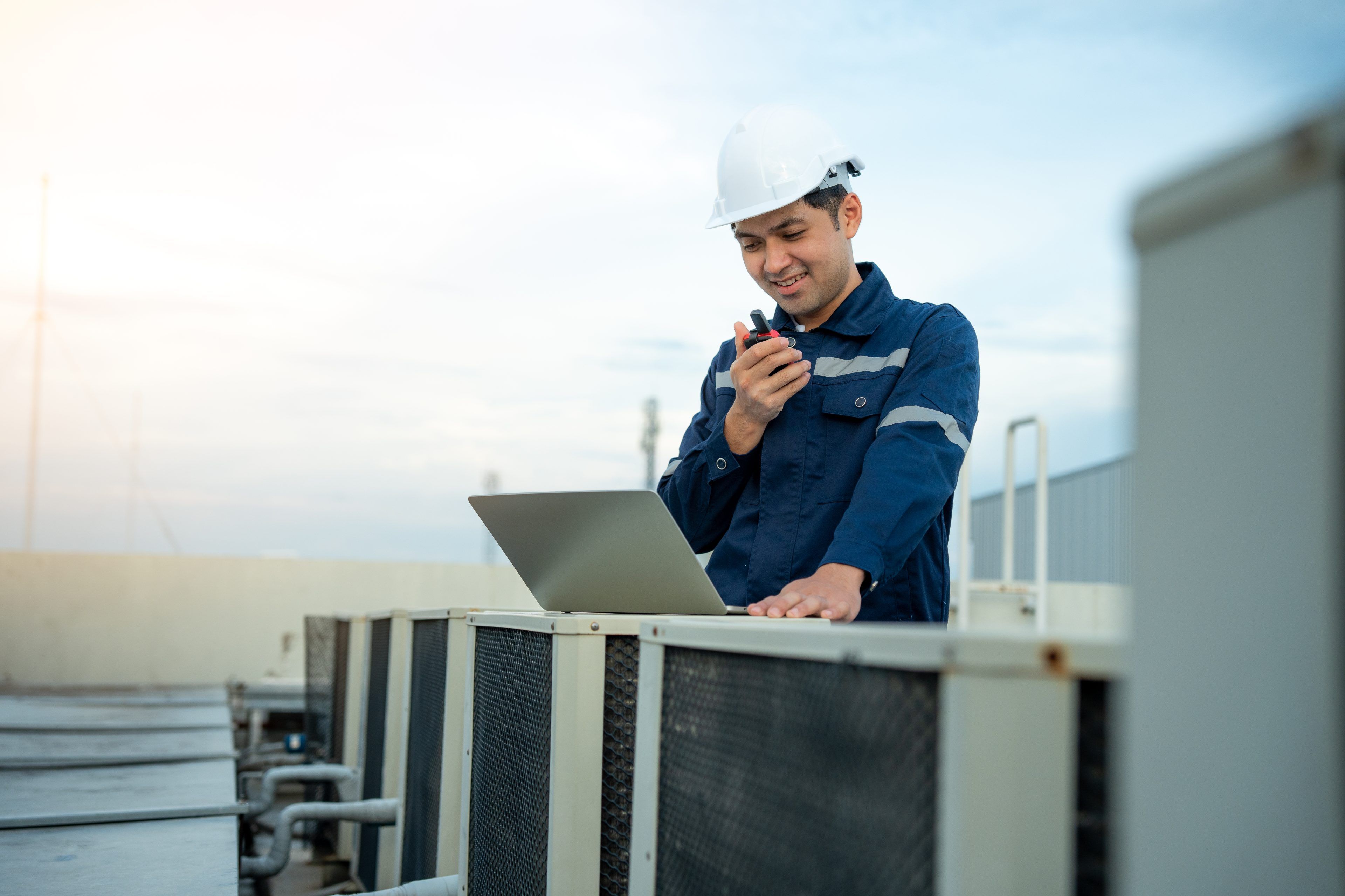 Asian maintenance engineer wear helmet works on the roof of factory. Supervisor inspect compressor system and plans installation of air condition systems in construction site of modern buildings.