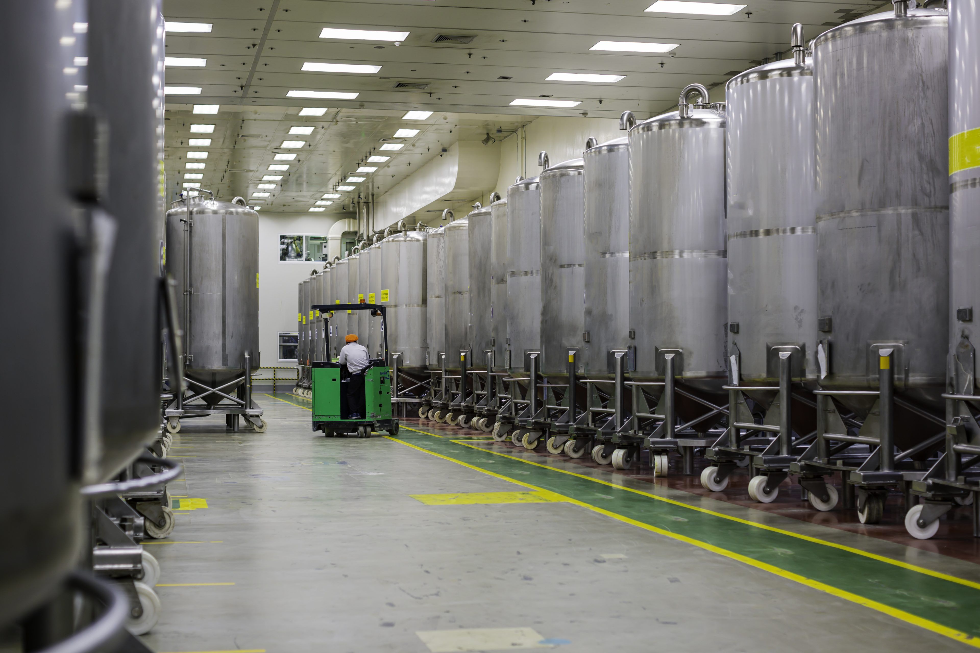 A male worker moving a bucket stainless vertical steel tanks equipment tank chemical cellar with scrolling wheel stainless steel tanks cleaning and treatment at shampoo factory.